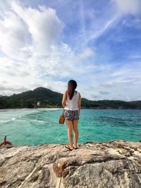 Rear view of young woman standing by sea against sky