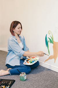 Caucasian woman artist hand painting murals on walls at apartment with acrylic paints