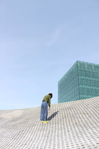Rear view of girl standing on tiled floor against blue sky