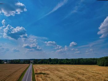 Empty road amidst field against blue sky