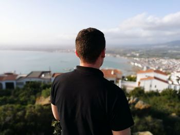 Rear view of man looking at cityscape against sky