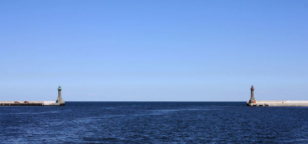 Lighthouse by sea against clear sky