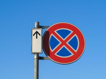 Low angle view of road sign against clear blue sky