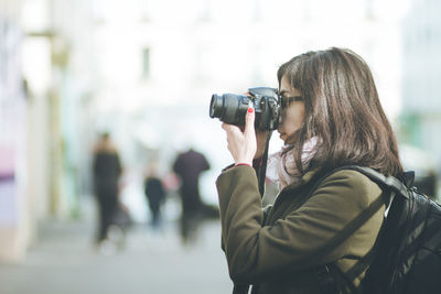 Side view of woman photographing with camera while standing in city