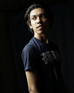 Portrait of young man standing against black background