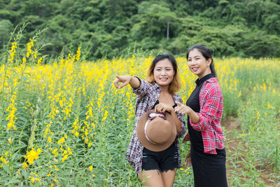 Smiling young woman standing by flowering plants on field