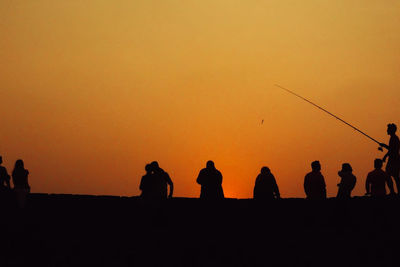 Silhouette people on field against orange clear sky during sunset