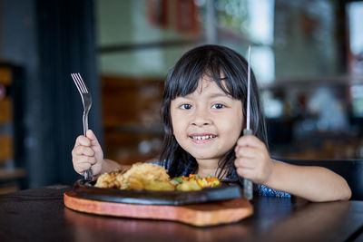 Close-up portrait of smiling girl with food on table in restaurant