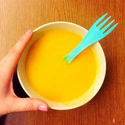 Cropped hand holding soup bowl on table