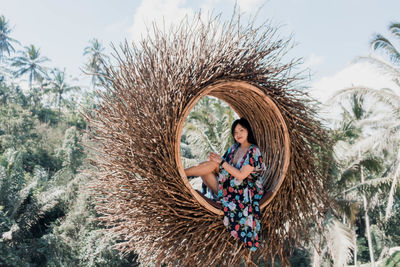 Pretty asian woman is sitting on straw nest, ubud, bali.