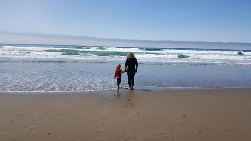 Rear view of woman standing with daughter at beach