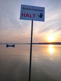 Information sign by sea against sky during sunset