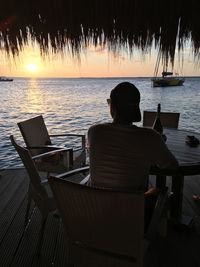 Rear view of man sitting on chair at sea