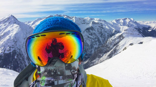 Close-up portrait of person wearing ski goggles with reflection against snowcapped mountains