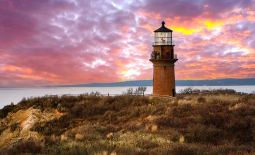 Lighthouse by sea against sky during sunset