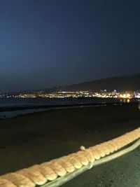 Illuminated city by sea against clear sky at night