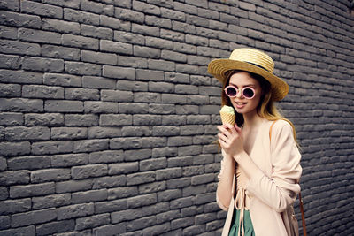 Young woman wearing sunglasses standing against brick wall