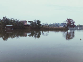 Reflection of trees and houses in lake against sky