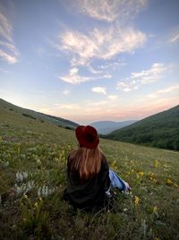 Rear view of woman sitting on rock against sky