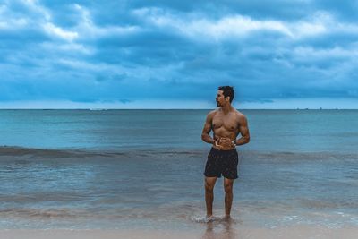 Full length of shirtless man standing at beach against sky