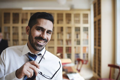 Portrait of happy male lawyer holding eyeglasses in library