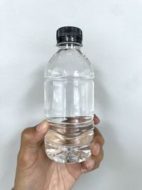 Close-up of hand holding glass bottle against white background