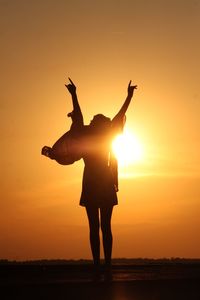 Silhouette woman  celebrating standing on beach against sky during sunset