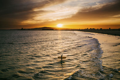 Surfer in sea at beach during sunset