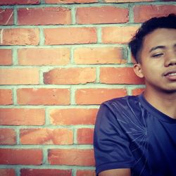 Young man looking away against brick wall