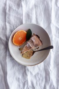 From above appetizing sweet cake and ripe orange mandarin cut and served on white plate on table