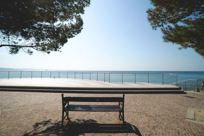 Empty bench by sea against clear sky