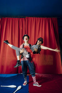Male clown carrying female performer while performing on circus stage