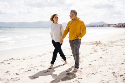 Smiling woman with man holding hands and walking on shore at beach