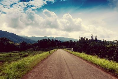 Empty road amidst field against sky