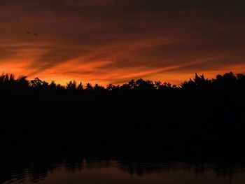 Silhouette trees by lake against romantic sky at sunset