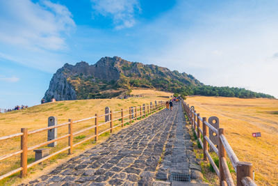 Rear view of people walking on footpath leading towards cliff