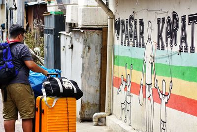 Rear view of man standing by graffiti on wall