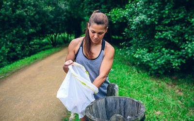 Young woman putting garbage in bin while standing on footpath