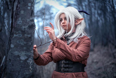 Portrait of young woman standing against tree trunk