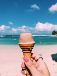 Midsection of person holding ice cream in sea against sky