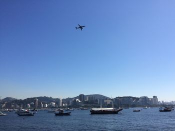 Boats in sea against clear blue sky and an airplane