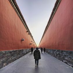 Rear view of man walking on footpath amidst buildings