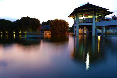 Built structure by lake against sky at dusk