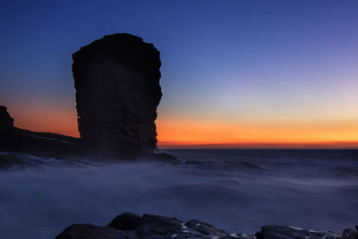Rock formation on beach against sky during sunset