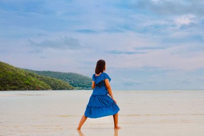 Rear view of woman standing on beach against sky