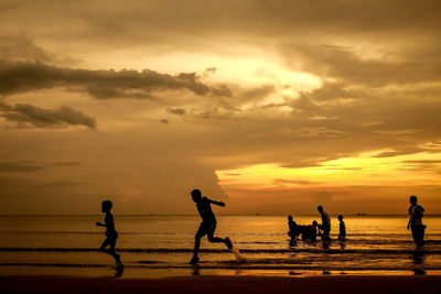 Silhouette people playing on beach against sky during sunset