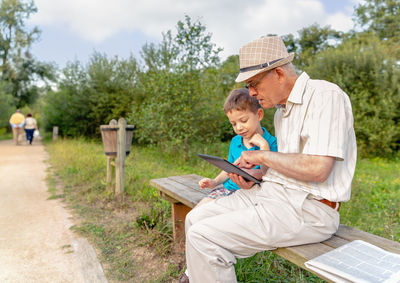 Grandson teaching digital tablet to grandfather while sitting in public park