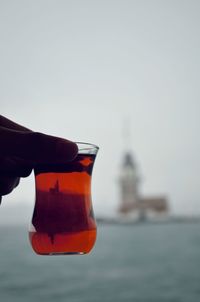 Close-up of hand holding bottle against sea against sky