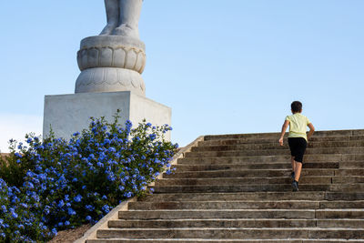 Low angle view of man walking on staircase against blue sky