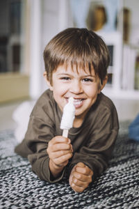 Portrait of smiling boy having ice cream while lying on carpet